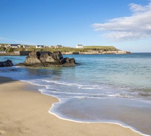 The water lapping the sandy beach at Ness, with houses and coastline across the water, Lewis.