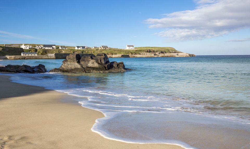 The water lapping the sandy beach at Ness, with houses and coastline across the water, Lewis.