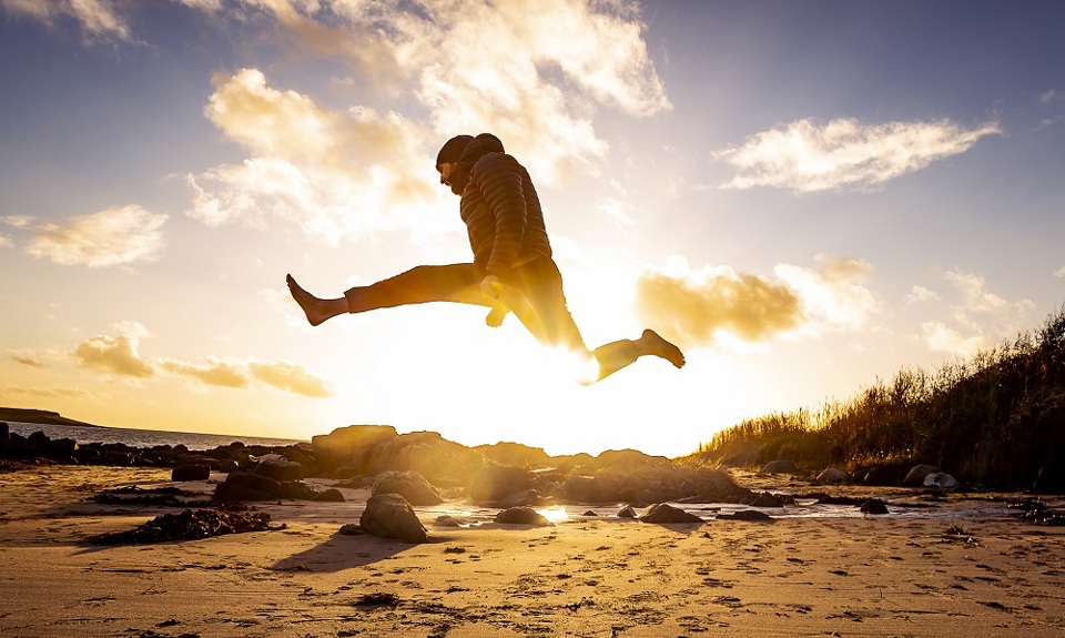 A man jumping in mid-airon a beach at sunset