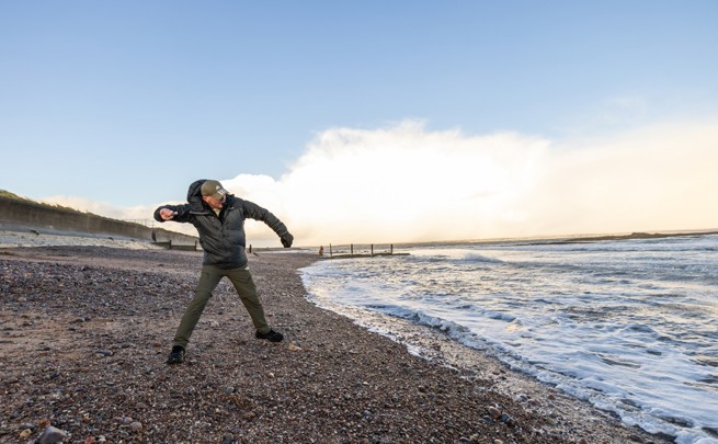 Man skimming stones into the sea, standing on a pebbled storeline in Portnaguran, Lewis