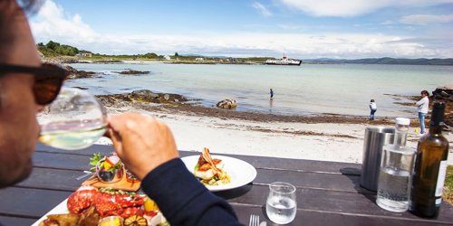 A male having a seafood lunch outdoors with a view of a CalMac Ferry on the coast