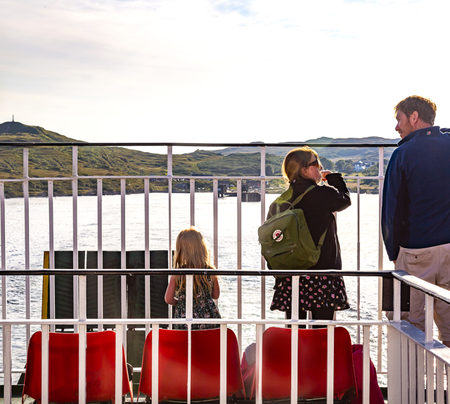 Father with two daughter on deck of ferry looking out to sea and sunshine