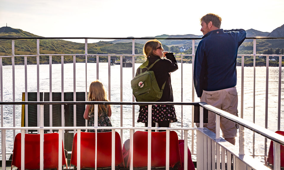 Father with two daughter on deck of ferry looking out to sea and sunshine