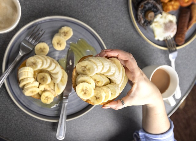 someone holding a bagel with banana drizzled in honey above their plate