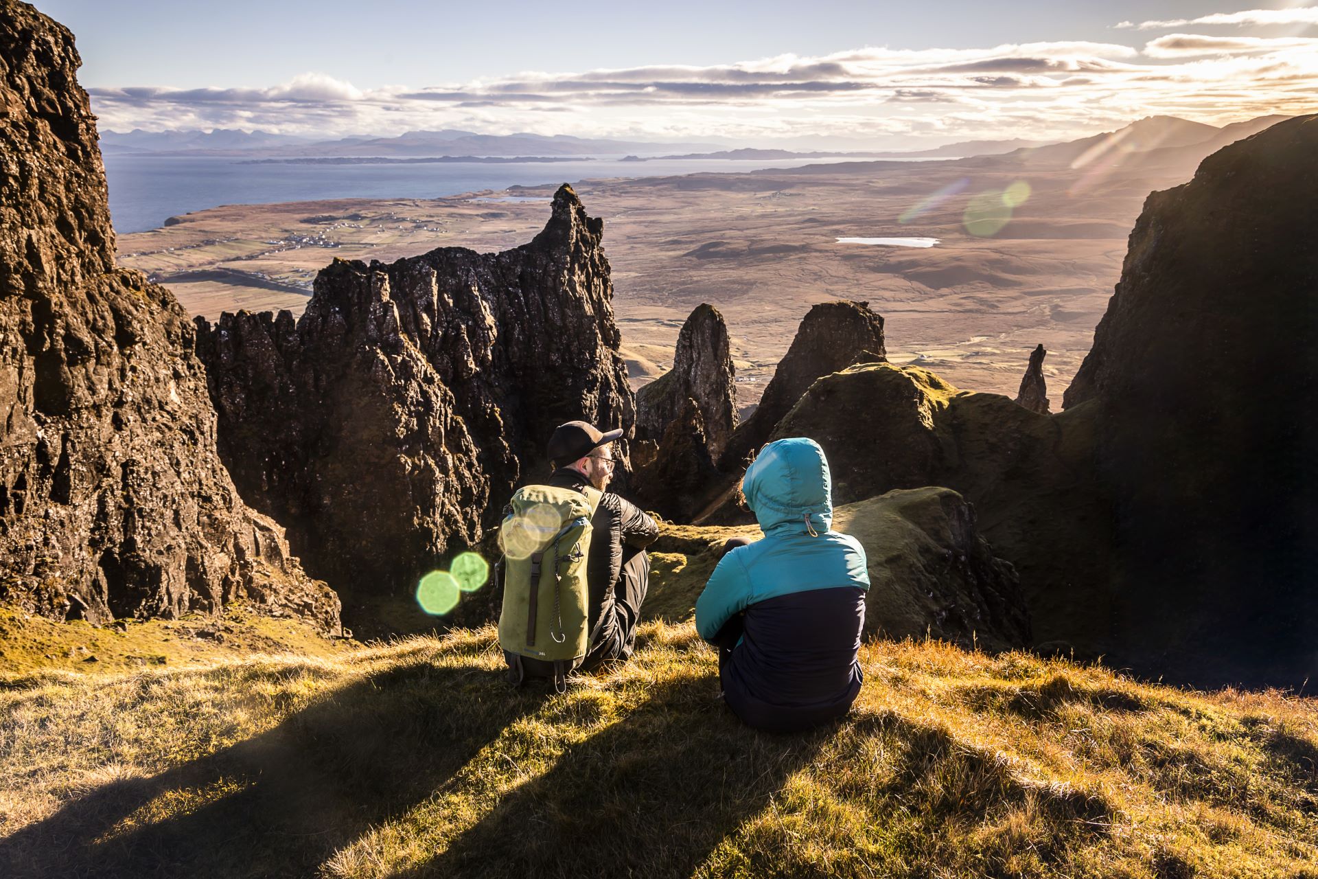 Hillwalkers resting with a view of mountain peaks and coastline, and across the water to the mainland from the Isle of Skye