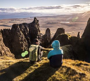 Hillwalkers resting with a view of mountain peaks and coastline, and across the water to the mainland from the Isle of Skye