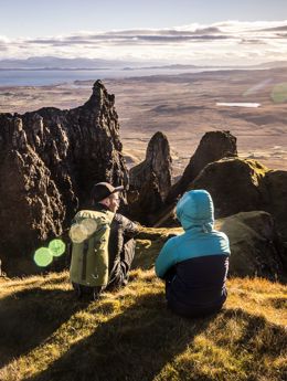 Hillwalkers resting with a view of mountain peaks and coastline, and across the water to the mainland from the Isle of Skye