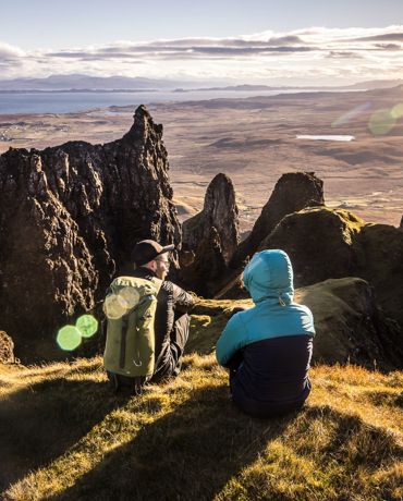 Hillwalkers resting with a view of mountain peaks and coastline, and across the water to the mainland from the Isle of Skye