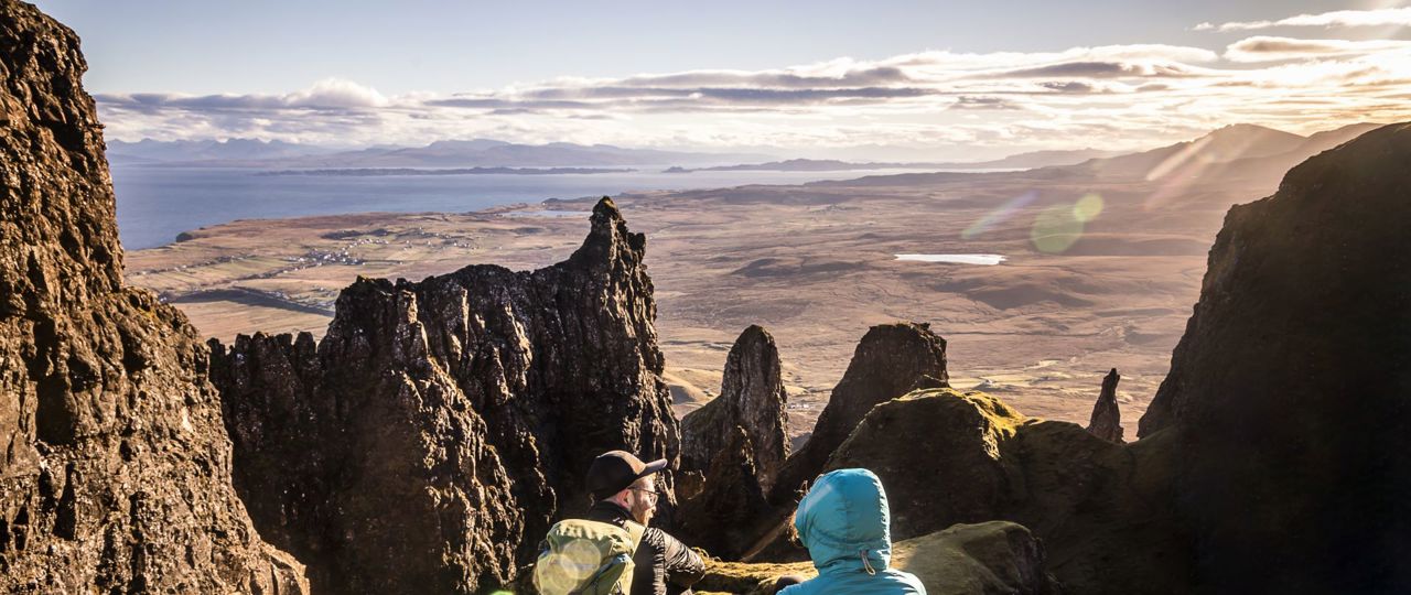 Hillwalkers resting with a view of mountain peaks and coastline, and across the water to the mainland from the Isle of Skye