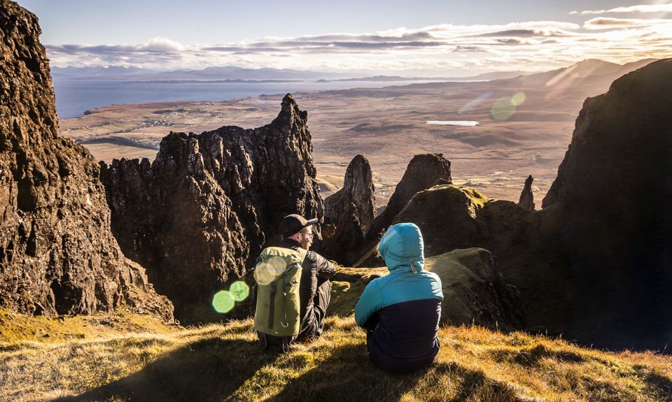 Hillwalkers resting with a view of mountain peaks and coastline, and across the water to the mainland from the Isle of Skye