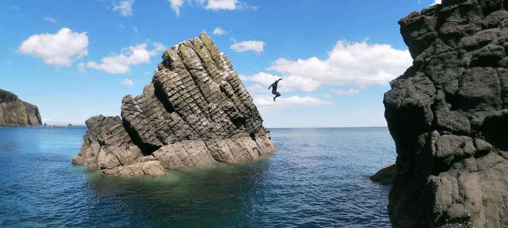 An adventurer jumping from a small rockface into the sea