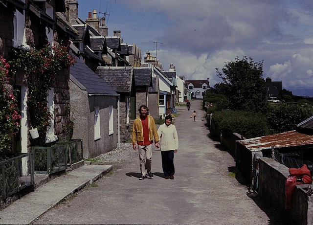 A man and woman holding hands, walking down a seaside village in Iona in the 1970's. 