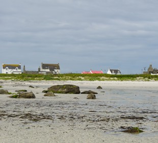White sand beach with scattered rocks and coastal cottages under a moody sky at low tide.