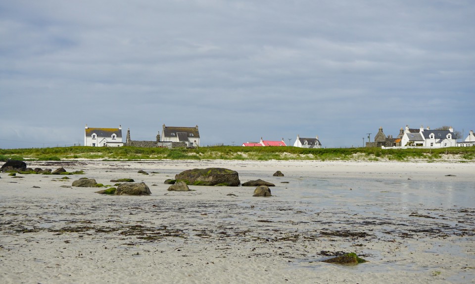 White sand beach with scattered rocks and coastal cottages under a moody sky at low tide.