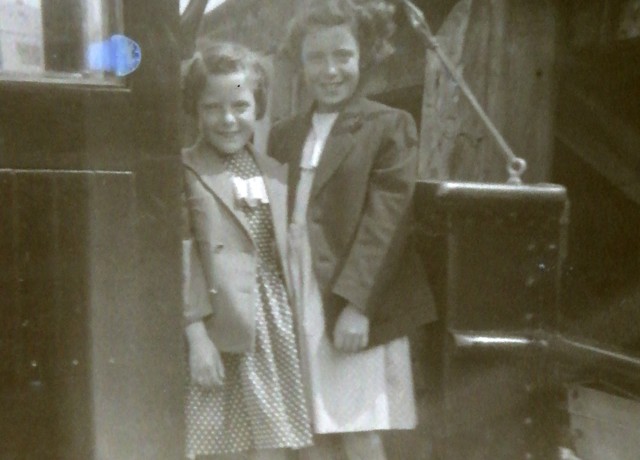 Black and white photo from 1950's of two young girls aged between 5 - 7yo. Standing on a boat smiling.