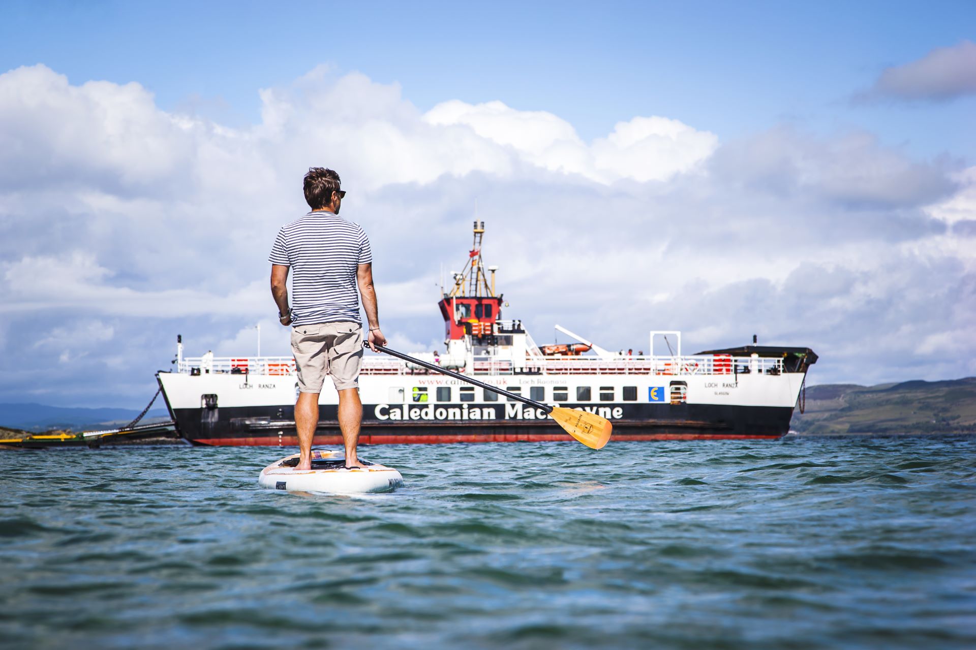 A man on the water on a stand up paddle board, admiring the CalMac ferry to Gigha