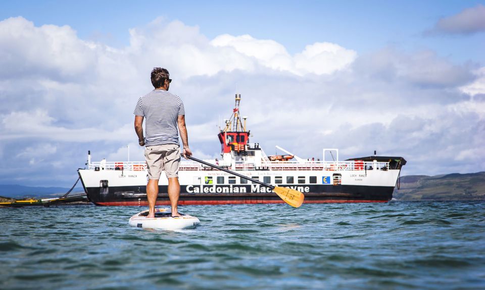 A man on the water on a stand up paddle board, admiring the CalMac ferry to Gigha