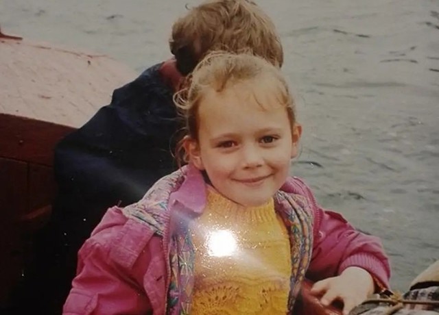 Photograph of a young girl aged about 7 years facing camera, smiling, on a fishing boat. Taken on a holiday to Barra in 1999.