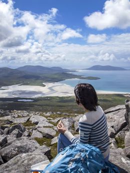 A hiker admiring the view down the rocky hillside to the golden sandy beaches and rolling hills in the distance