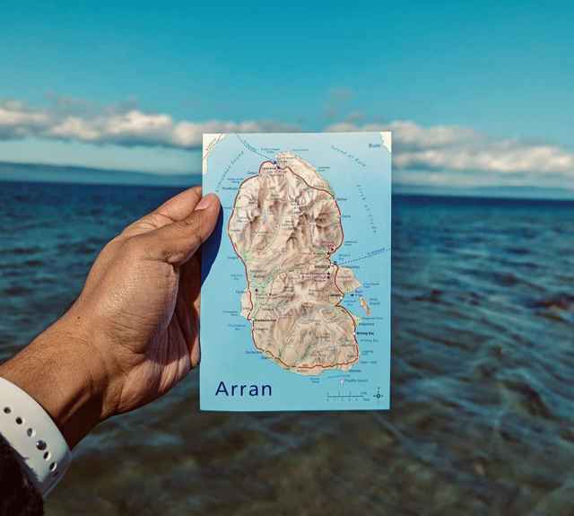 A hand holding a postcard size map of Arran