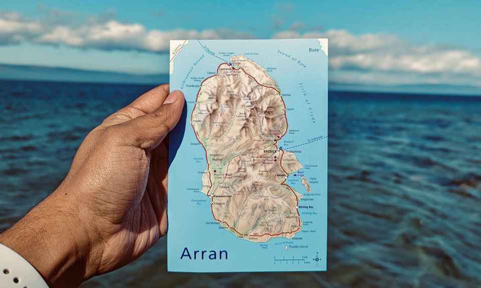 A hand holding a postcard size map of Arran