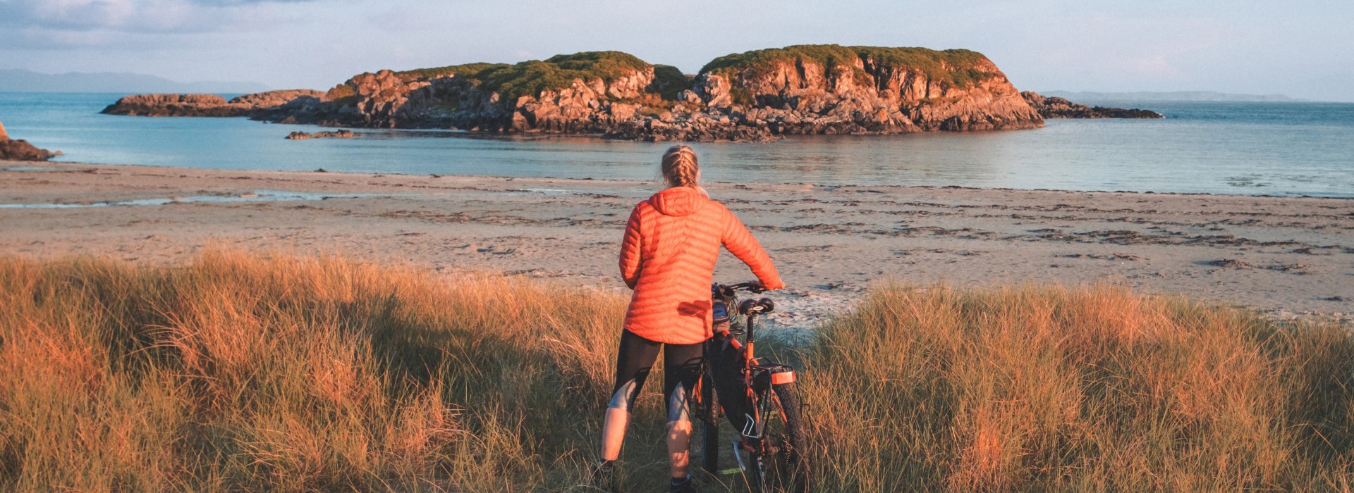 A cyclist with their bike on the beach, looking out across the water.
