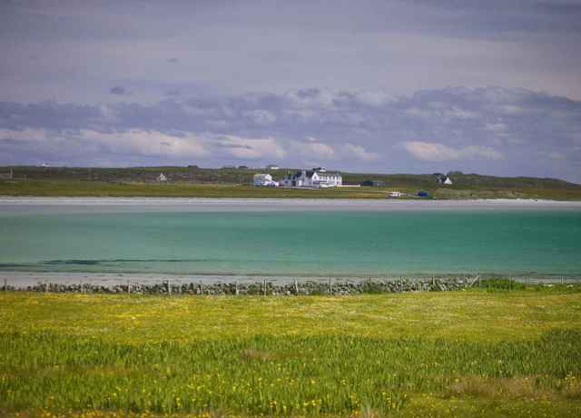 View across the colourful green grass and turquoise waters of Gott Bay to a hotel on Tiree.