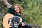 Nati Galloway being filmed while playing a guitar with her left arm in the air