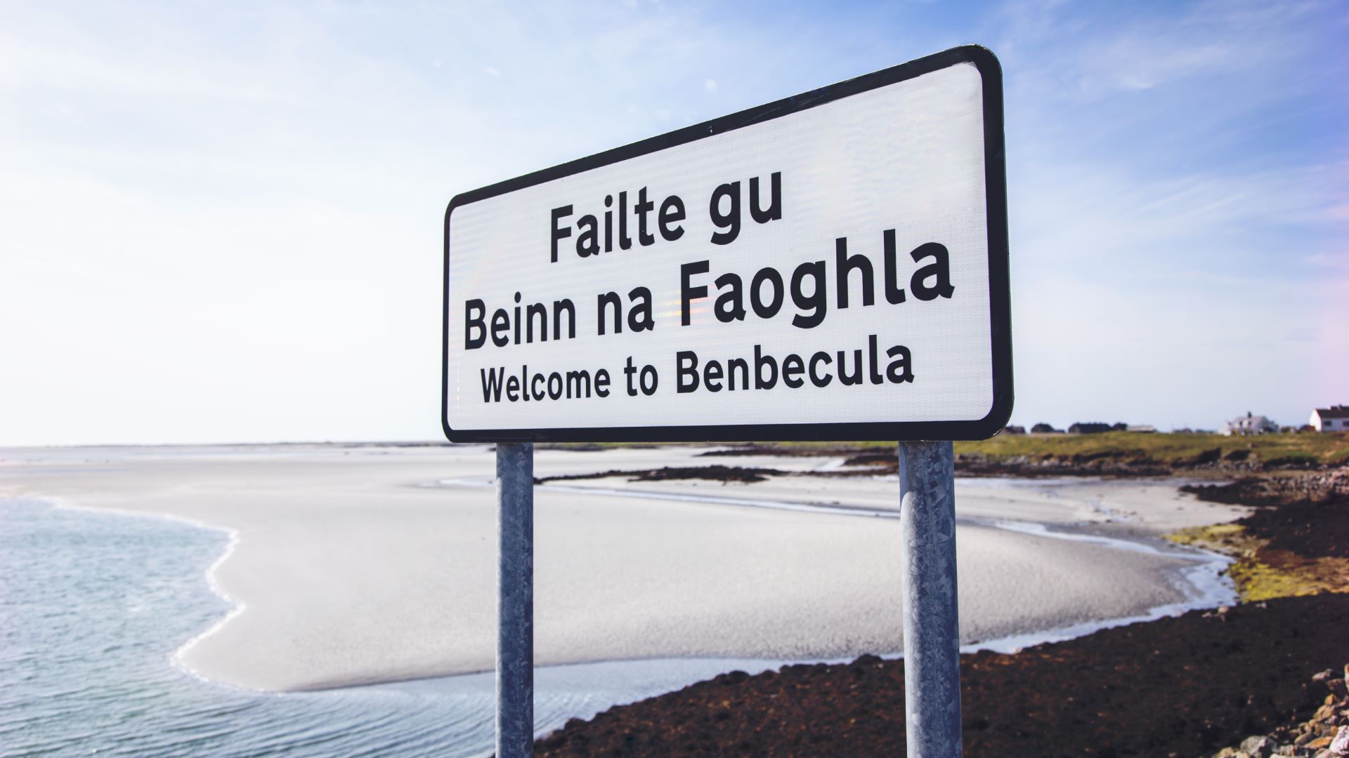 Welcome to Benbecula sign with Gaelic language version, with a white sandy beach in the background.