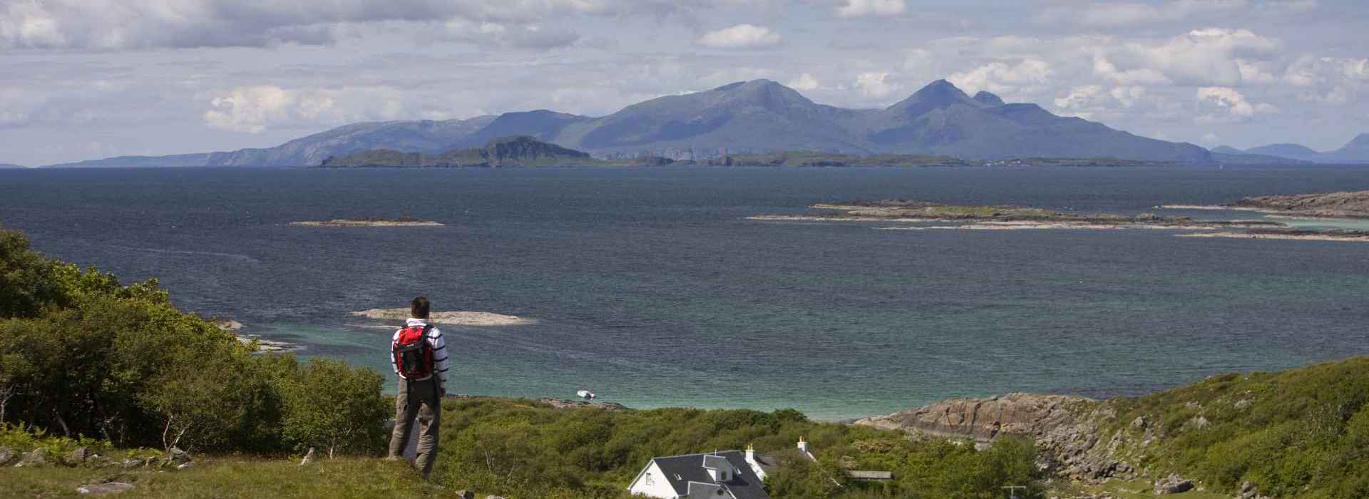 A man standing looking across the sea towards the island of Rum from Ardnamurchan.