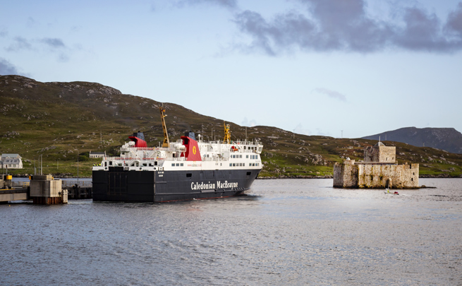 The Caledonian MacBrayne ferry to Barra sitting in the bay next to the rugged stone Kisimul Castle.