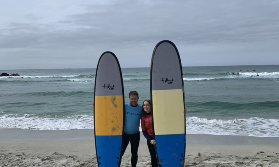 two surfers posing on the beach each holding a surfboard