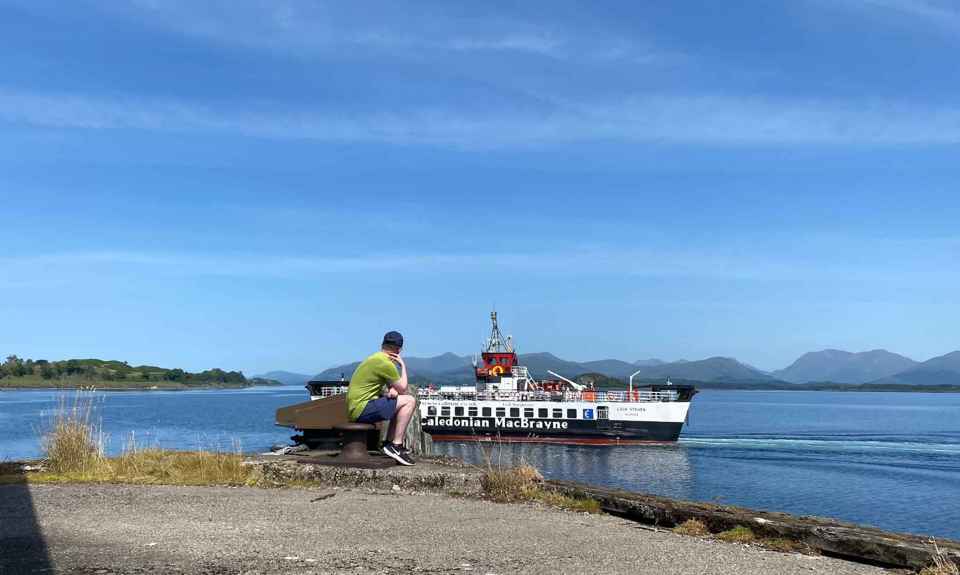 A Caledonian MacBrayne (CalMac) ferry sails to Lismore, with a person looking on from the harbour. Lismore.