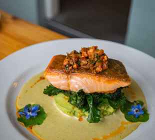 A restaurant prepared salmon fillet on a bed of vegetables with a creamy sauce.