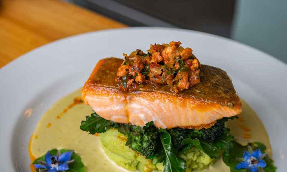 A restaurant prepared salmon fillet on a bed of vegetables with a creamy sauce.