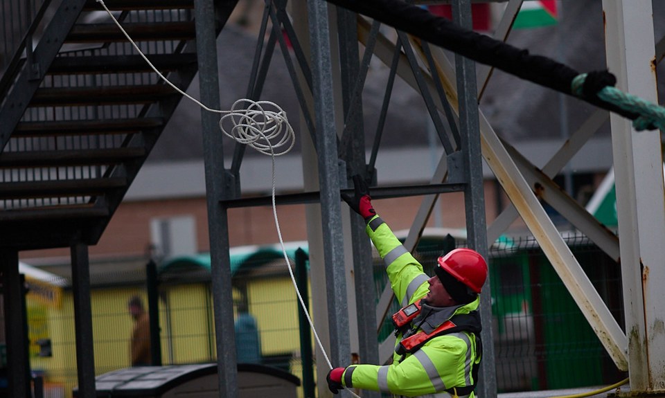 Port operative on the quayside handling a heaving line beside ferry infrastructure at Oban harbour.