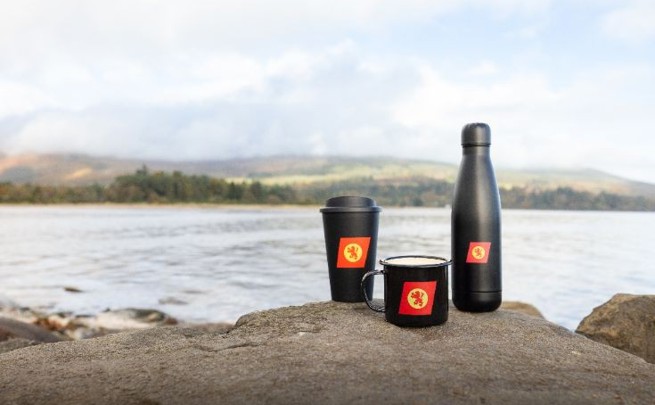 CalMac branded cups and bottle sitting on a rock by the sea.