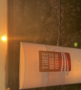 branded Tiree Music Festival cup with the sunset in the background. 