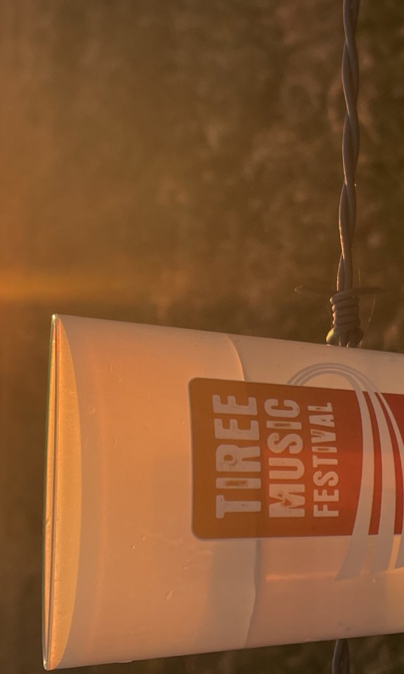 branded Tiree Music Festival cup with the sunset in the background. 