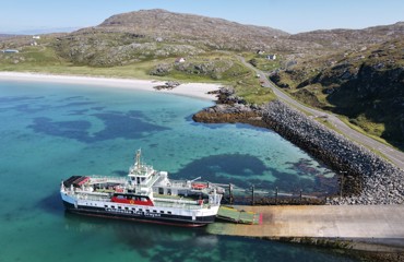 the MV Loch Alainn berthed at Eriskay with the blue water and white sand to the left and the causeway to the right