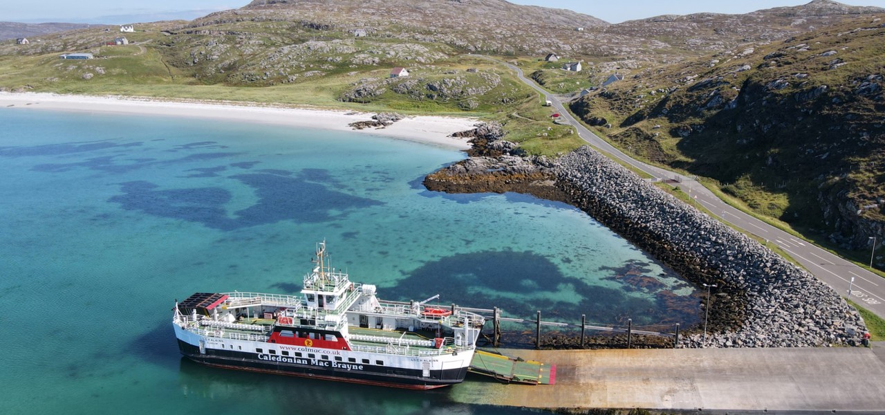 the MV Loch Alainn berthed at Eriskay with the blue water and white sand to the left and the causeway to the right