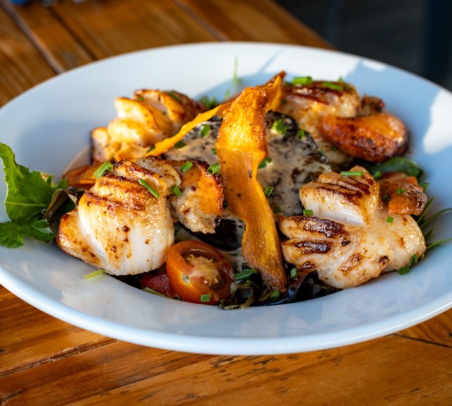 a plate of scallops on a white plate sitting on a wooden table 