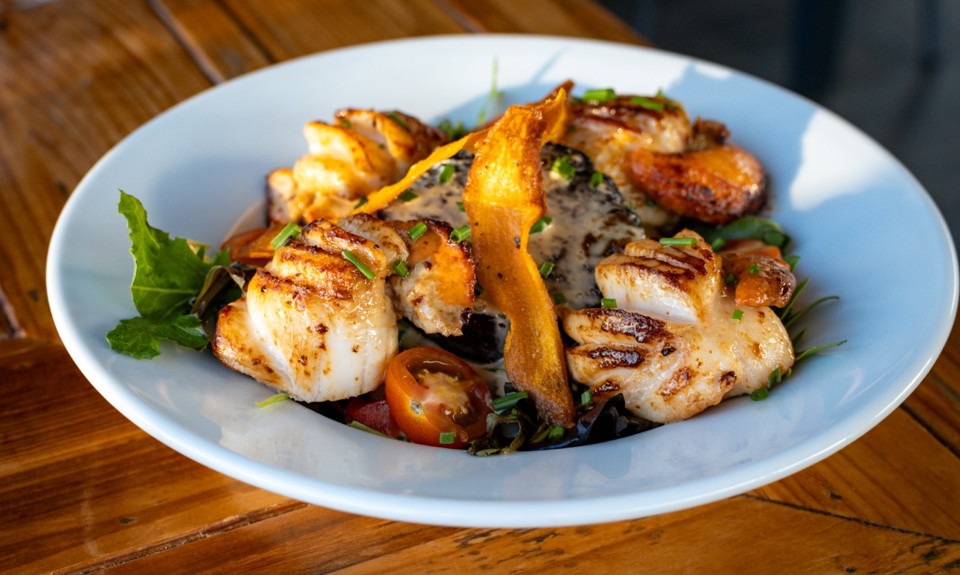 a plate of scallops on a white plate sitting on a wooden table 