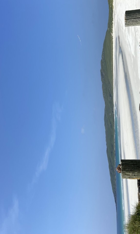 steel gate leading to a beach with white sand and blue water