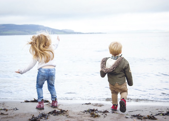 Two young kids on the beach throwing rocks into the sea