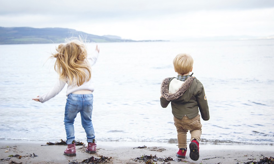 Two young kids on the beach throwing rocks into the sea