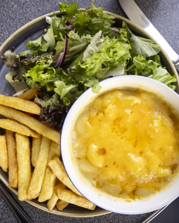 A plate of food consisting of a bowl of macaroni cheese, a serving of fries, and a portion of mixed green salad. 