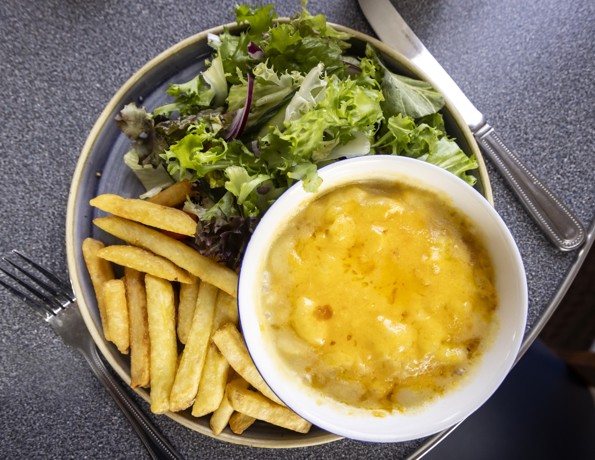 A plate of food consisting of a bowl of macaroni cheese, a serving of fries, and a portion of mixed green salad. 