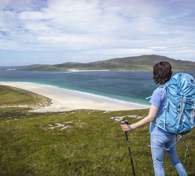 A hiker admiring the view down to the golden sandy beaches and rolling hills in the distance