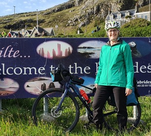 Person in green jacket with bike at 'Welcome to the Hebrides' sign.